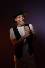Fototapeta premium Talented young man singing on dark background with color light