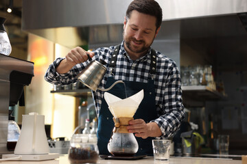 Barista brewing coffee in glass coffeemaker with paper filter at table in cafe