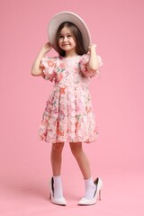 Stylish little girl wearing oversized high heeled shoes on pink background