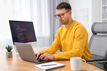 Programmer working on laptop at wooden desk indoors