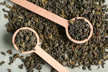 Wooden spoons with dry green tea leaves on grunge green background