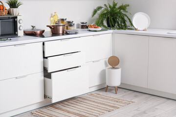 Interior of modern kitchen with stylish rug, trash bin and white counters