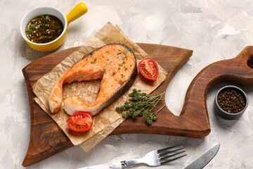 Wooden board of tasty salmon steak on grey background