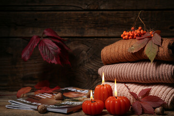 Beautiful autumn composition with burning candles in shape of pumpkin and sweaters on wooden...