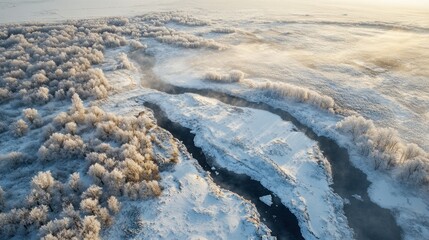 Aerial view of a snow-covered river winding through a frost-covered forest at sunrise.