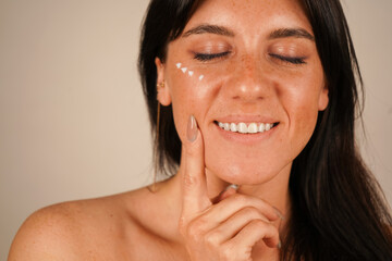 She spreads moisturizer over her face with her fingertips, emphasizing hydration and nourishment.