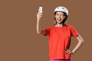 Beautiful young woman in helmet taking selfie on brown background