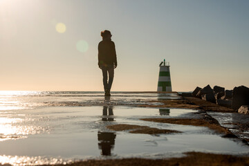 silhouette of a woman walking along a causeway to a lighthouse with reflections in the water