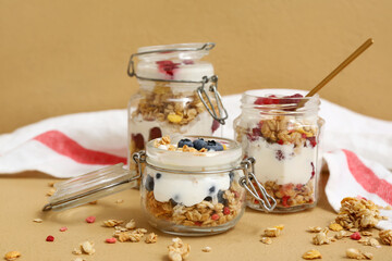 Jars of tasty granola with yogurt and berries on beige background