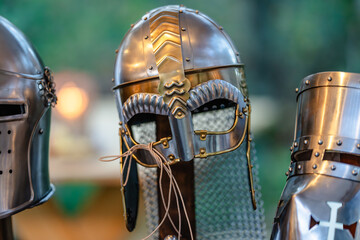 Three medieval helmets are displayed, one of which has a mask on it