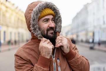 Bearded man wearing winter clothes adjusting hood in city street