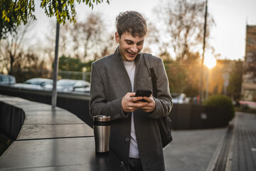 Fototapeta premium young adult man stand with thermos and use mobile phone on the street