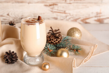 Glass of tasty eggnog cocktail with cinnamon, pine cones, fir branch and Christmas balls on white wooden background