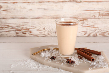 Glass of tasty eggnog cocktail with star anise and cinnamon on white wooden background