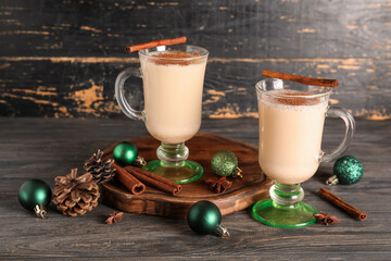 Glasses of tasty eggnog cocktail with cinnamon, star anise, pine cones and Christmas balls on black...