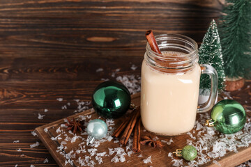 Mason jar of tasty eggnog cocktail with cinnamon, star anise and Christmas balls on wooden background