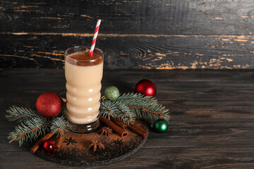 Glass of tasty eggnog cocktail with cinnamon, star anise, fir branches and Christmas balls on black...