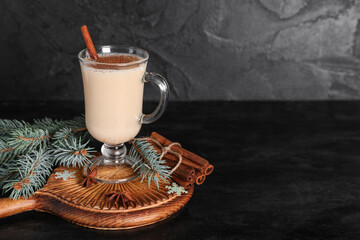 Glass of tasty eggnog cocktail with cinnamon, star anise and Christmas tree branches on black...