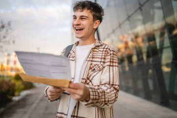 Young adult man student open and read files from envelope outdoor
