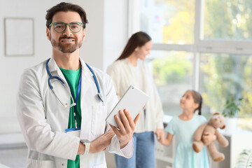 Fototapeta premium Male pediatrician with tablet computer against girl with mother in clinic