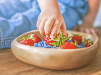 child's hand reached for a ripe strawberry, which lies in a wooden saucer