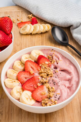 Smoothie bowl on a wooden board with fresh fruit and granola toppings