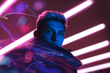 Stylish young man illuminated by blue and pink neon lights with dynamic streaks and futuristic...