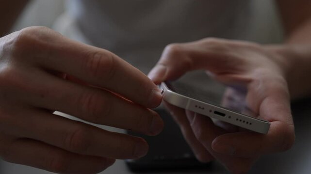 Male fingers extracting small sim card from modern smartphone with metallic ejection tool, demonstrating wireless communication device maintenance. Process of changing or replacing the sim, close-up.