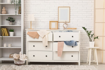 Interior of messy living room with shelving unit, scattered clothes and commode