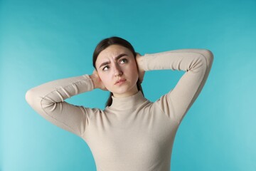Distressed woman covering her ears from loud noise on blue background