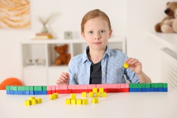 Little girl playing with colorful cubes at white table indoors