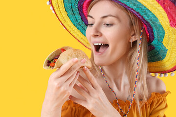Young woman in sombrero hat eating tasty taco on yellow background, closeup