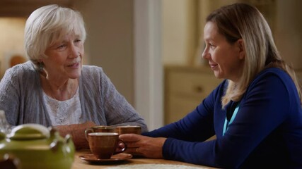 Two women sit at a wooden table, engaged in a heartfelt conversation. One woman enjoys tea from a cup while the other listens intently, creating a cozy and inviting atmosphere