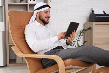 Arab businessman working with tablet computer on armchair in office
