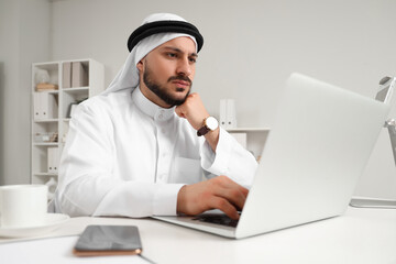 Thoughtful Arab businessman working with laptop at table in office