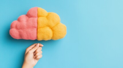 A hand gently holds a felted cloud, divided into pink and yellow sections, symbolizing creativity and ideas