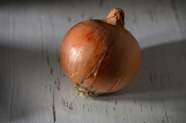 Brown onion rests on a rustic surface, lit naturally, showcasing its texture and imperfections