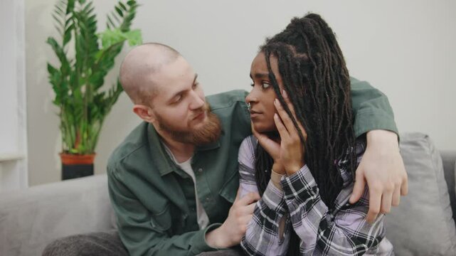 husband gently comforts his An African-American wife as she sits sadly on the couch. He offers his love and support, creating a moment of emotional connection and reassurance at home