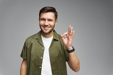 Young man smiling and showing okay gesture in casual outfit against neutral background