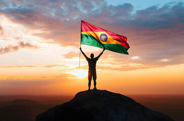Mozambique flag being waved by a man celebrating success at the top of a mountain against sunset or sunrise. Mozambique flag for Independence Day.