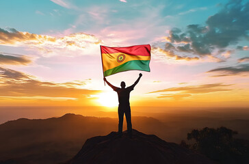 Mozambique flag being waved by a man celebrating success at the top of a mountain against sunset or sunrise. Mozambique flag for Independence Day.