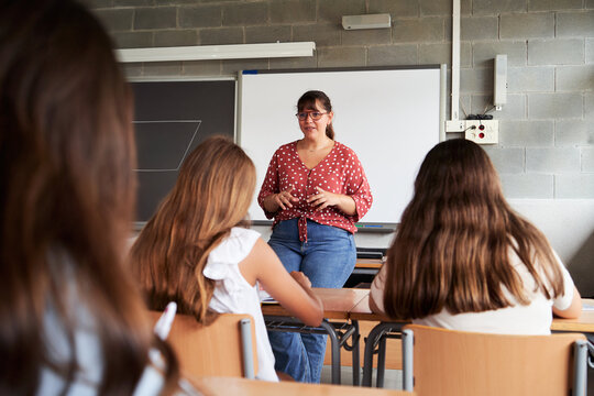 Female professor teaching in front of elementary school students in a classroom. Image with copy space.