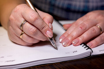 woman filling in diary, beautiful hands with manicure and ballpoint pen close-up