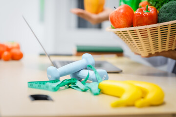 An Asian male nutritionist with a beard, wearing a lab coat, sits at a desk for an online consultation. His workspace includes fruits, vegetables, laptop, health supplements, promoting wellness.