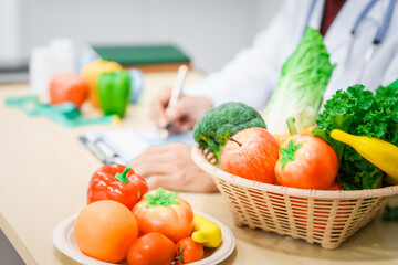 An Asian male nutritionist with a beard, wearing a lab coat, sits at a desk for an online consultation. His workspace includes fruits, vegetables, laptop, health supplements, promoting wellness.