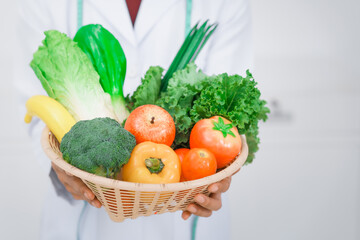 Close-up of a male nutritionist and health consultant in a lab coat, holding a basket filled with kale, bok choy, apple, tomato, broccoli, and leeks, healthy eating habits on a white background.
