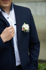 Groom adjusting navy blue suit jacket, white shirt, floral boutonniere, hand with ring, wedding attire concept