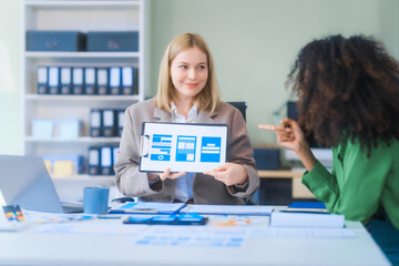 A young African American woman and a young Russian woman work together in a business office. They...