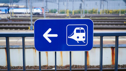 Sign directing passengers to train platform at busy railway station in urban area