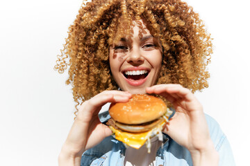 Naklejka premium Cheerful young woman with curly hair enjoying a delicious burger, representing healthy eating with a vibrant, white background